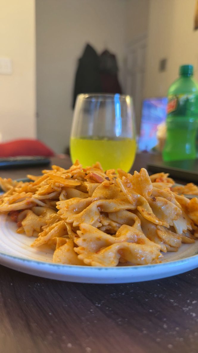 A plate of bow-tie pasta with a bright drink in a glass