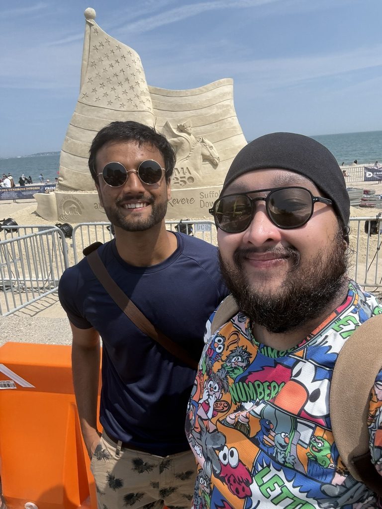 Dave and a friend in front of a sand sculpture by the water