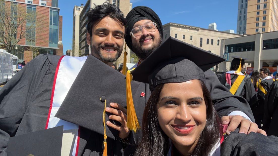 Dave in cap and gown with two friends at graduation